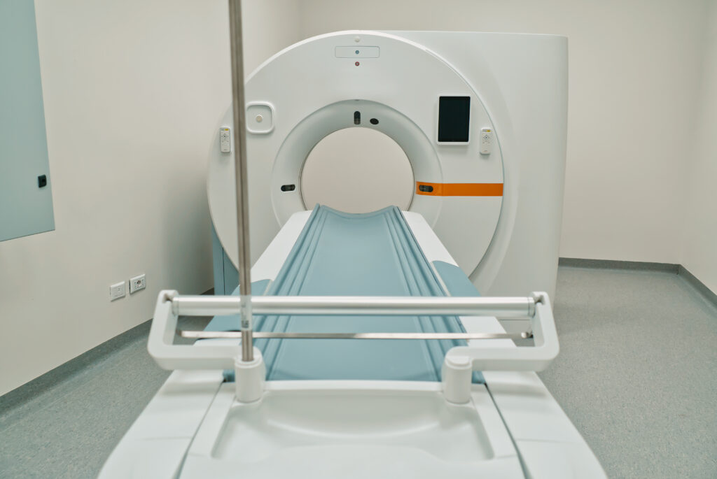 Uno scanner TC moderno in un ambiente clinico, dotato di una grande unità di scansione circolare con un tavolo piatto e imbottito di blu. La stanza è pulita e ha pareti e pavimenti di colore neutro.
