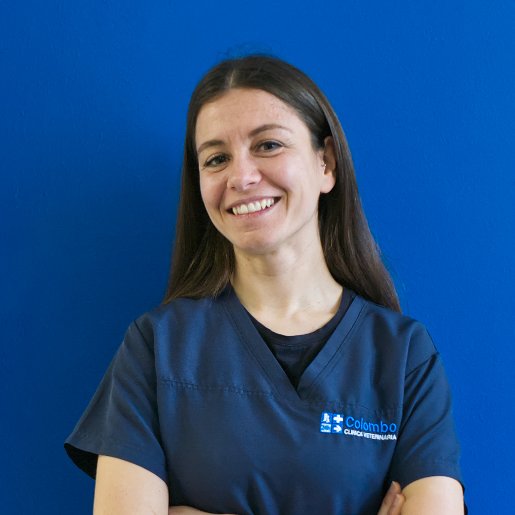 Una donna sorridente con lunghi capelli castani è in piedi su uno sfondo blu brillante, incarnando lo spirito di 