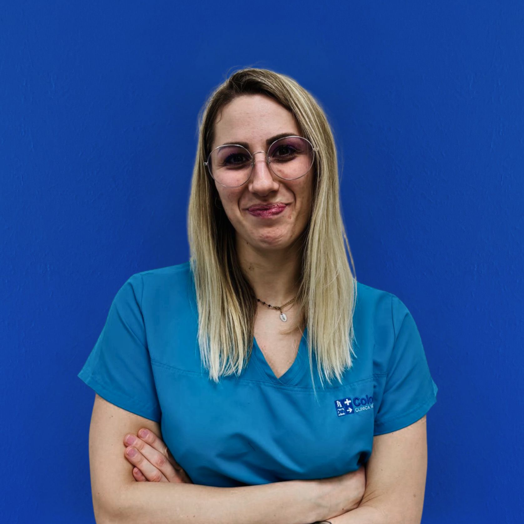 Il team di esperti include una donna con lunghi capelli biondi e occhiali, in piedi con sicurezza con le braccia incrociate in camice medico turchese su uno sfondo blu uniforme. Il suo leggero sorriso trasuda calore e professionalità.
